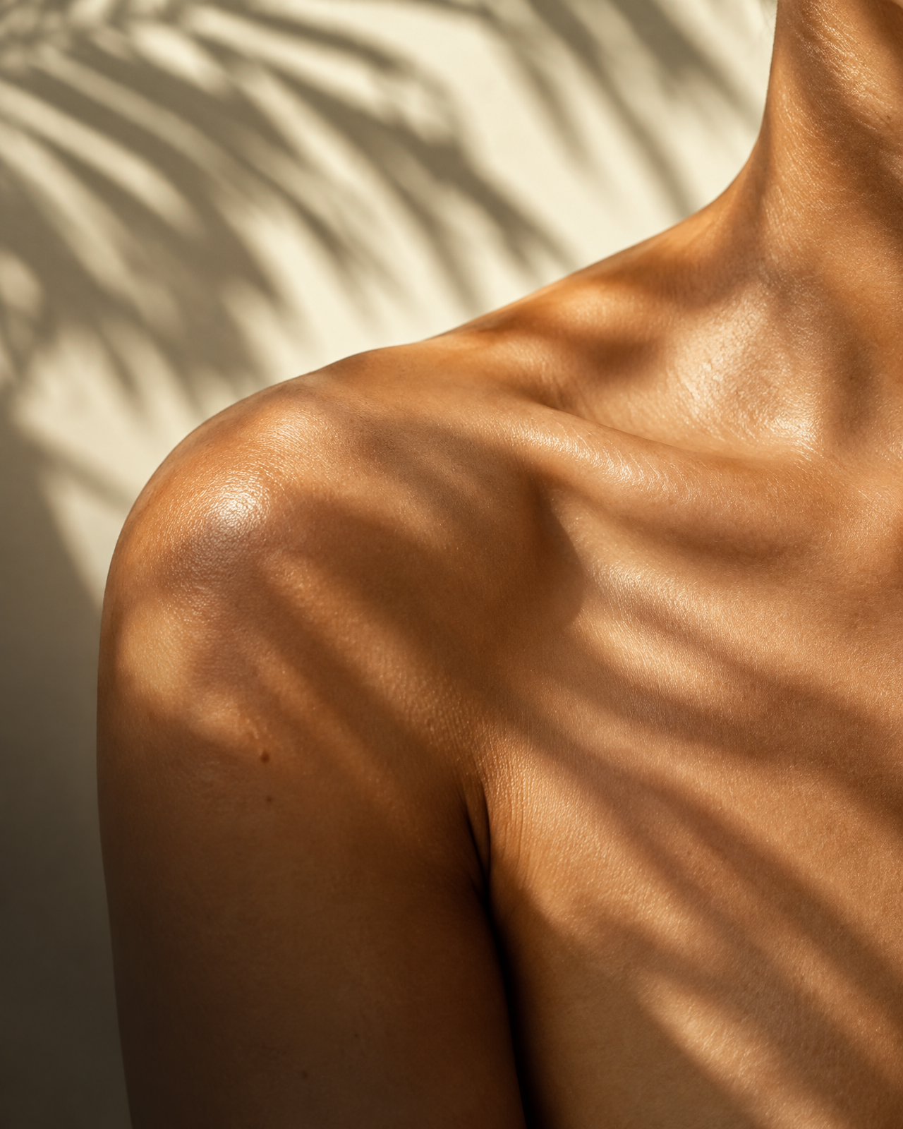 Shoulder and collarbone in dappled sunlight through palm leaves